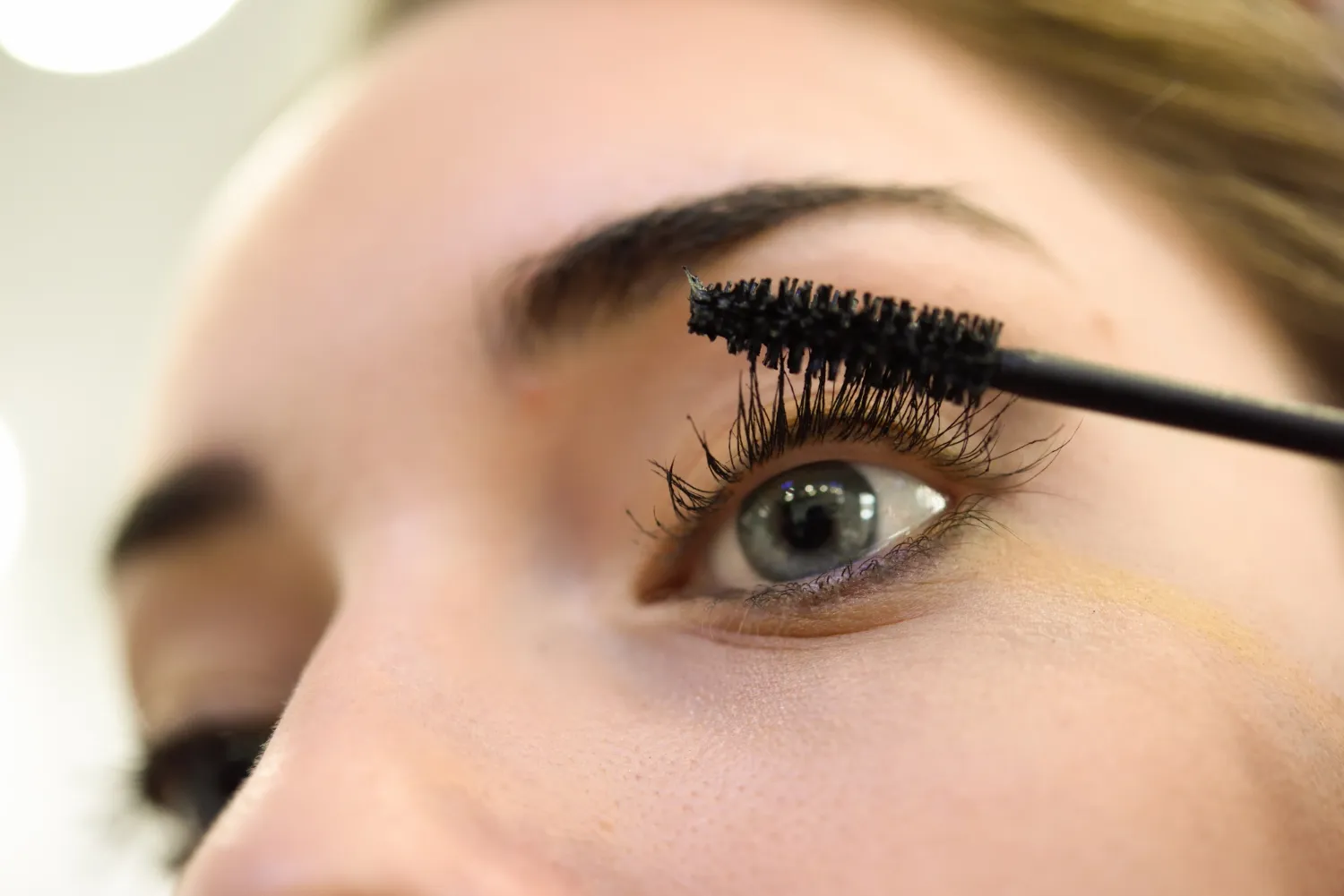 Mujer aplicando máscara de pestañas en un ojo, resaltando la belleza y el cuidado personal.